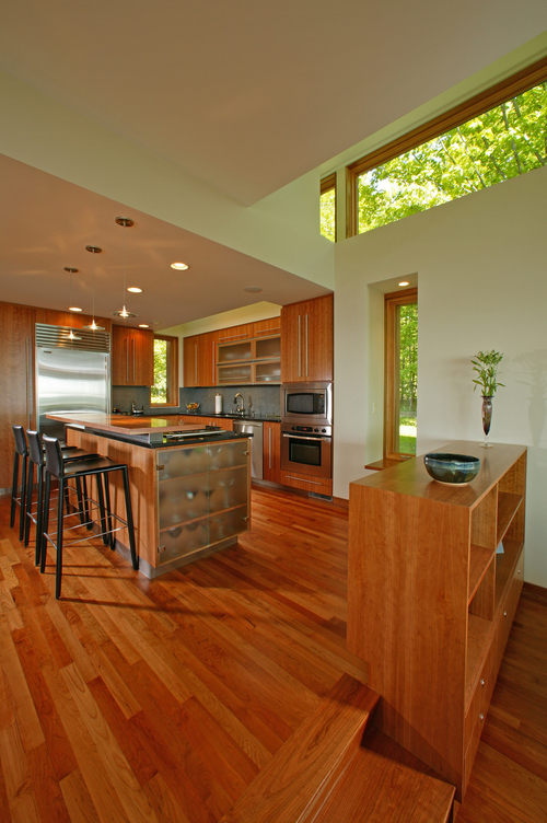 Kicthen demonstrates a simple design of the cupboards, appliances, and island. The wood elements create a warm atmosphere, and the huge windows let in plenty of natural light.