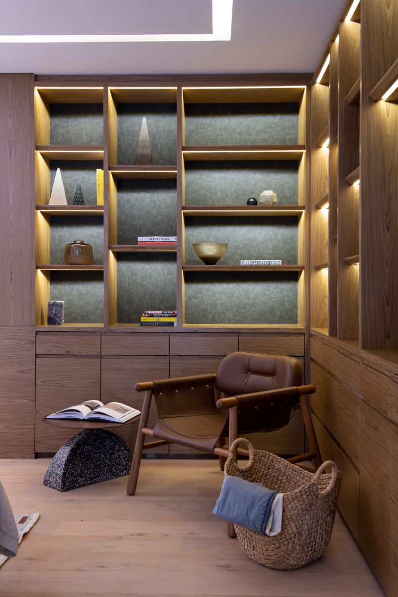 The reading area features a custom-built chair and table, light wood flooring, and open shelving constructed of natural wood.