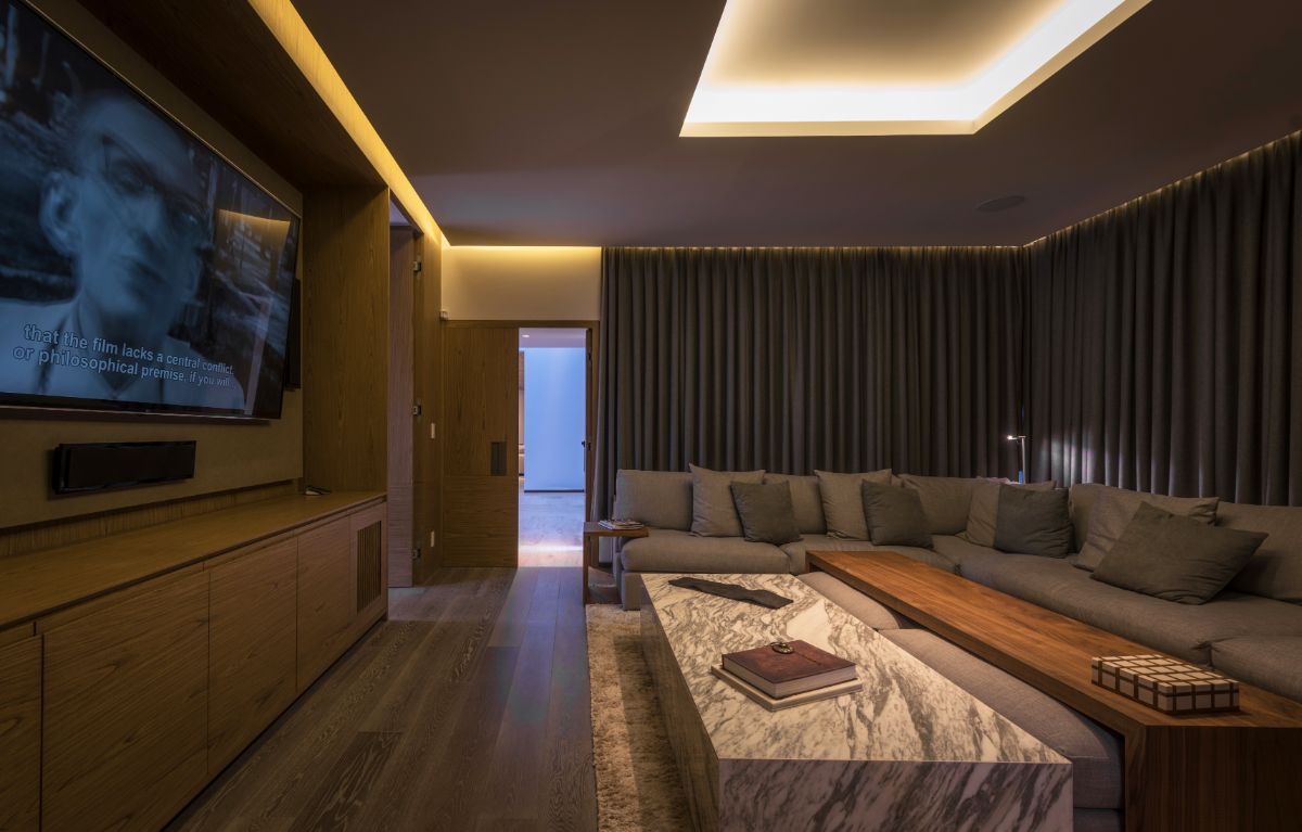 Warm hues on the floor, furniture, and walls in the TV room due to the wood materials, which contrast with the smooth and elegant fixed marble desk.