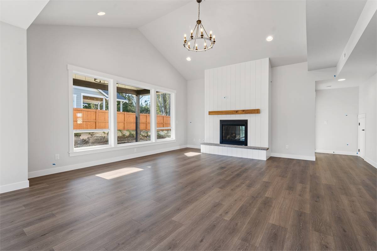 The great room has a cathedral ceiling, a fireplace, and a trio of windows overlooking the covered patio.