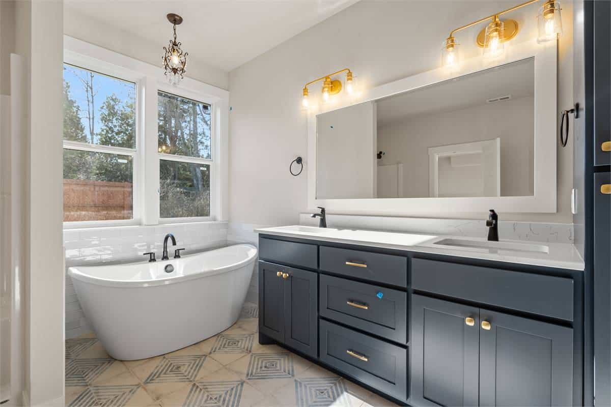 The primary bathroom has a freestanding tub and a dual sink vanity well-lit by brass sconces.