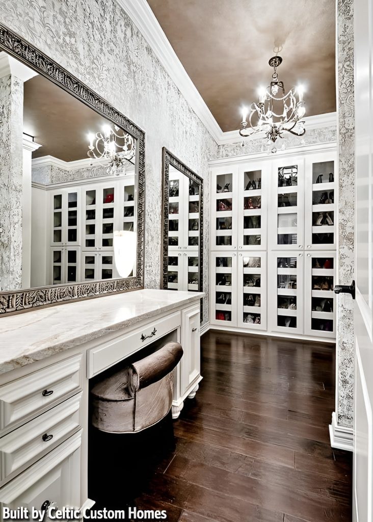 Walk-in closet with glass front cabinets and a marble top vanity paired with a velvet stool and large framed mirror.