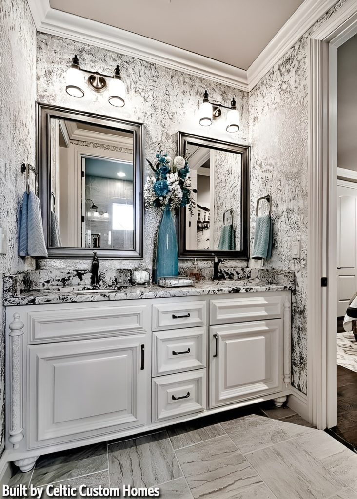 Powder room with dual sink vanity complemented by framed mirrors and glass sconces fixed against the gray patterned wallpaper.