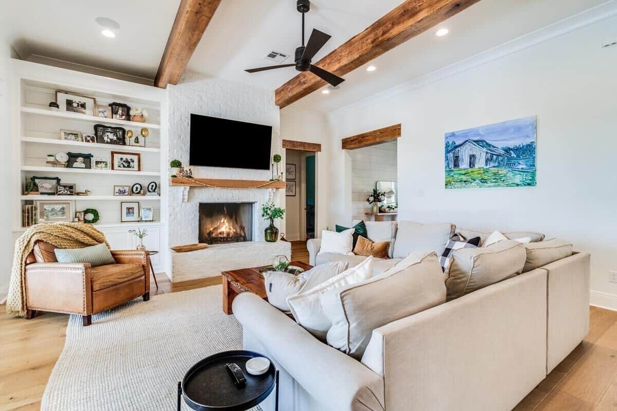 Living room with a beamed ceiling, gray sofas, and a leather armchair by the fireplace.