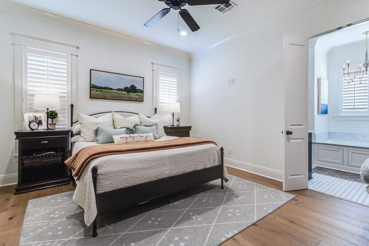 Primary bedroom with hardwood floor and double white doors unveiling the ensuite bath.