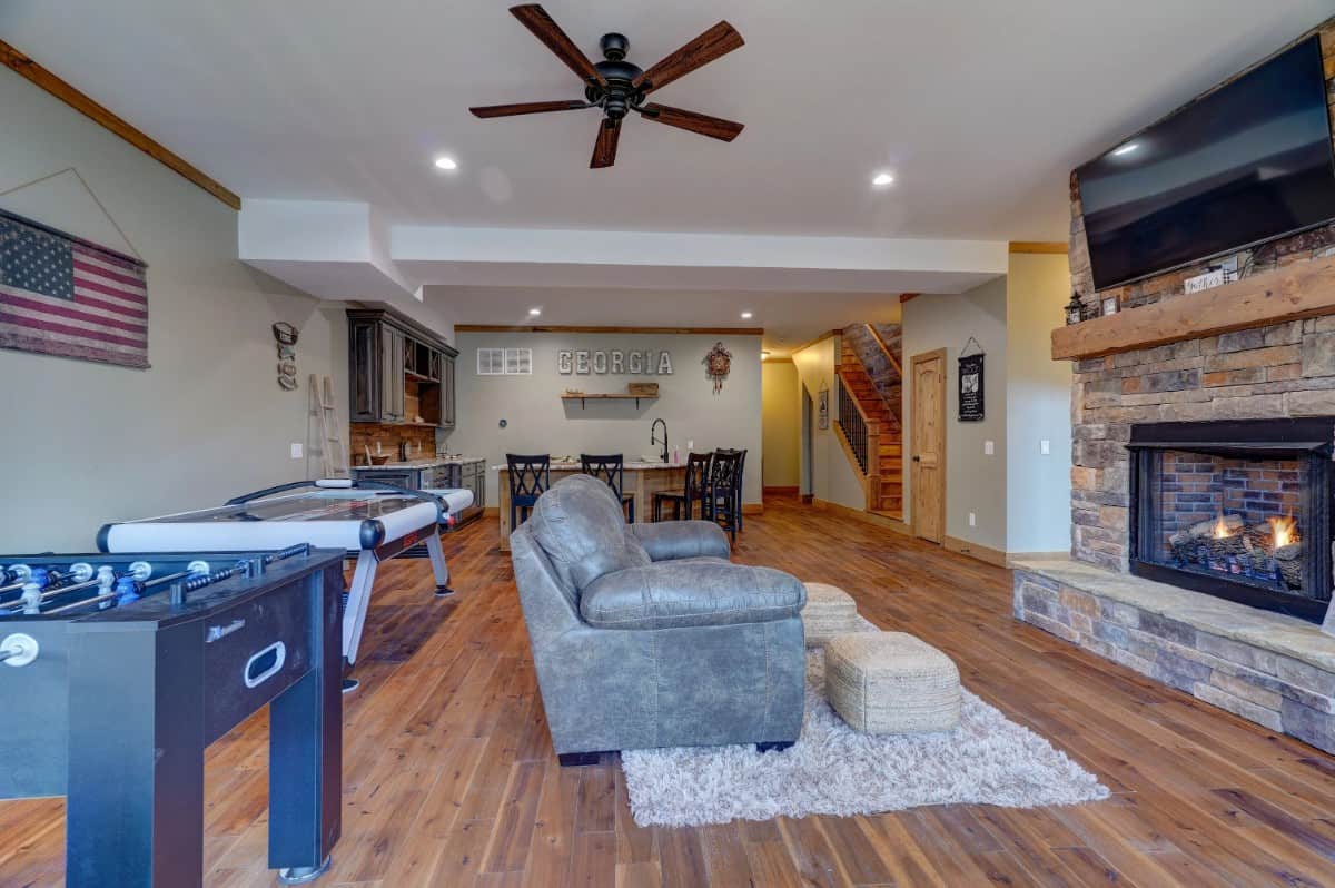 Social room with game tables, a leather sofa, and a TV mounted above the stone fireplace.