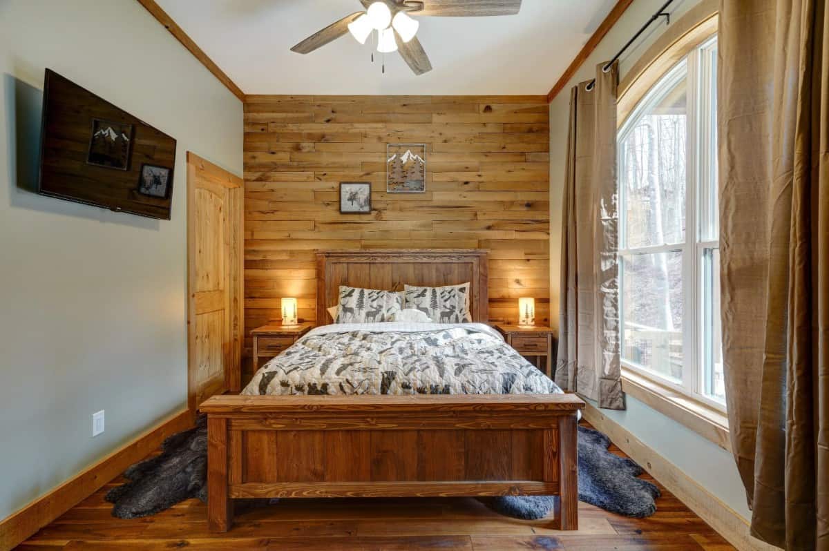 This bedroom has a wall-mounted TV and a wooden bed that blends in with the wood-paneled accent wall and hardwood floor.