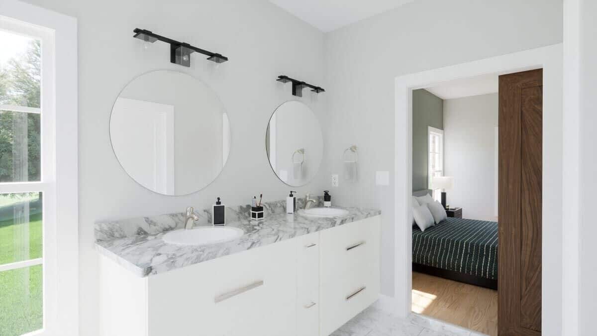 Primary vanity with two sinks, a marble countertop, and round mirrors topped with glass sconces.