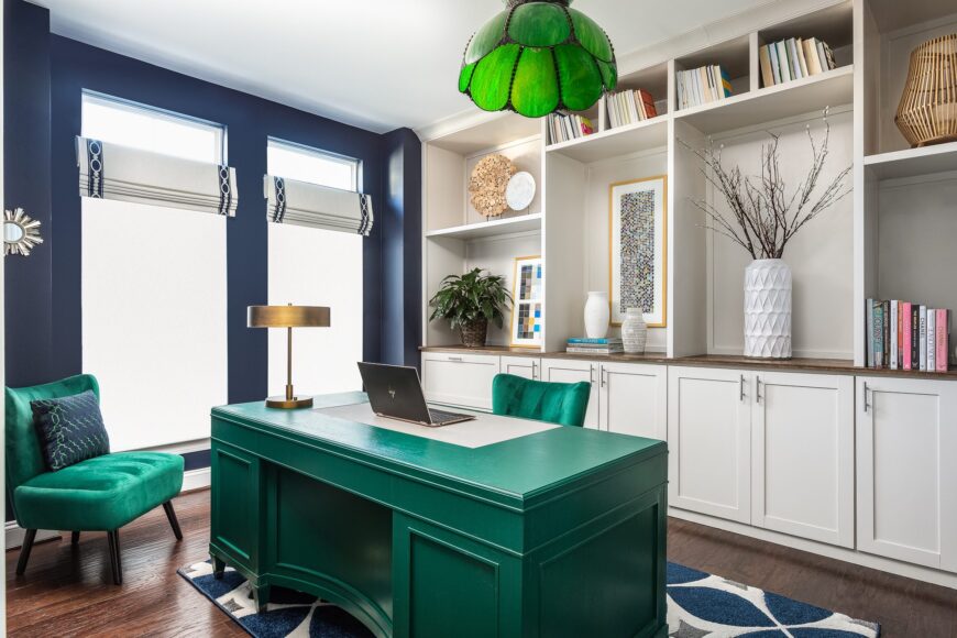 This captivating home office is the epitome of elegance and productivity. Bathed in sophistication, the emerald velvet desk and guest chairs exude luxurious comfort. The floor-to-ceiling built-in cabinets in the background showcase a curated collection of books and tastefully arranged vases, inspiring both creativity and intellectual pursuits.