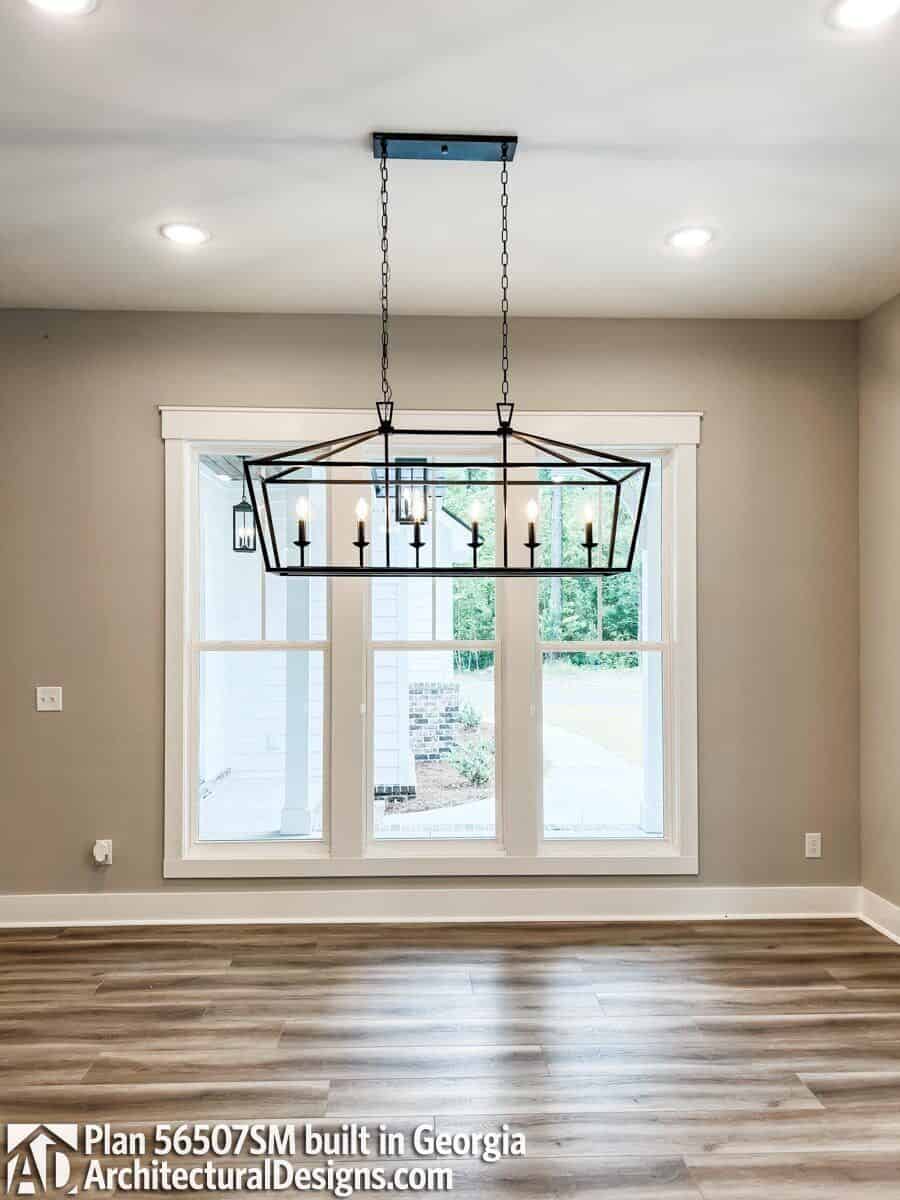 A trio of windows, recessed ceiling lights, and a wrought iron chandelier illuminate the dining room.