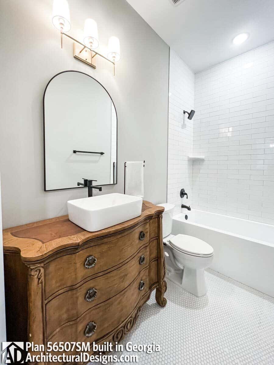 This bathroom offers a tub and shower combo and a wooden vanity with a vessel sink and an arched mirror.