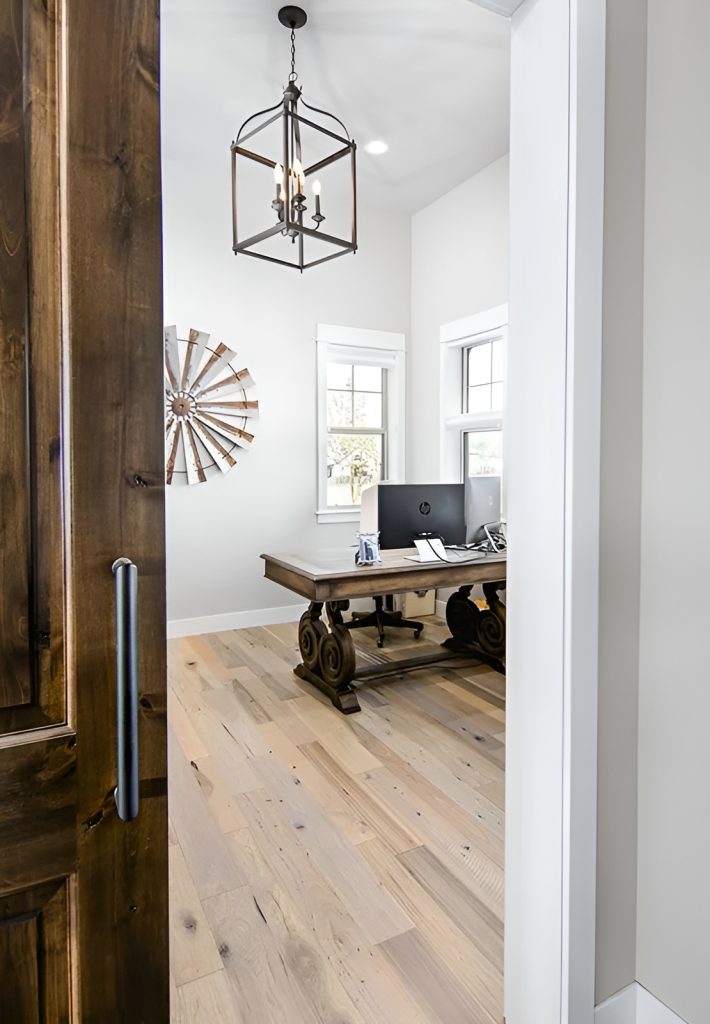 Home office with a large caged pendant, a wooden desk, and around artwork adorning the stark white walls.