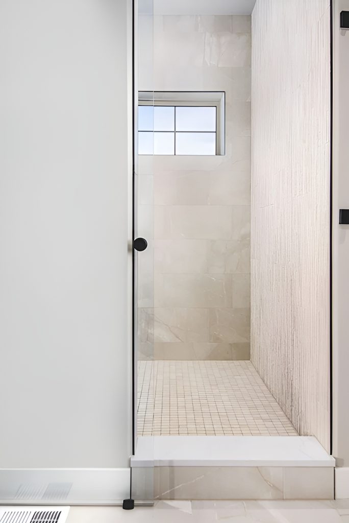 Walk-in shower with tiled walls, a glass hinged door, and a window that lets natural light in.