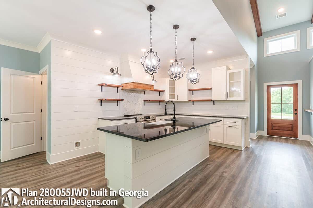 Kitchen with white cabinetry, floating shelves, and a center island fitted with a prep sink.