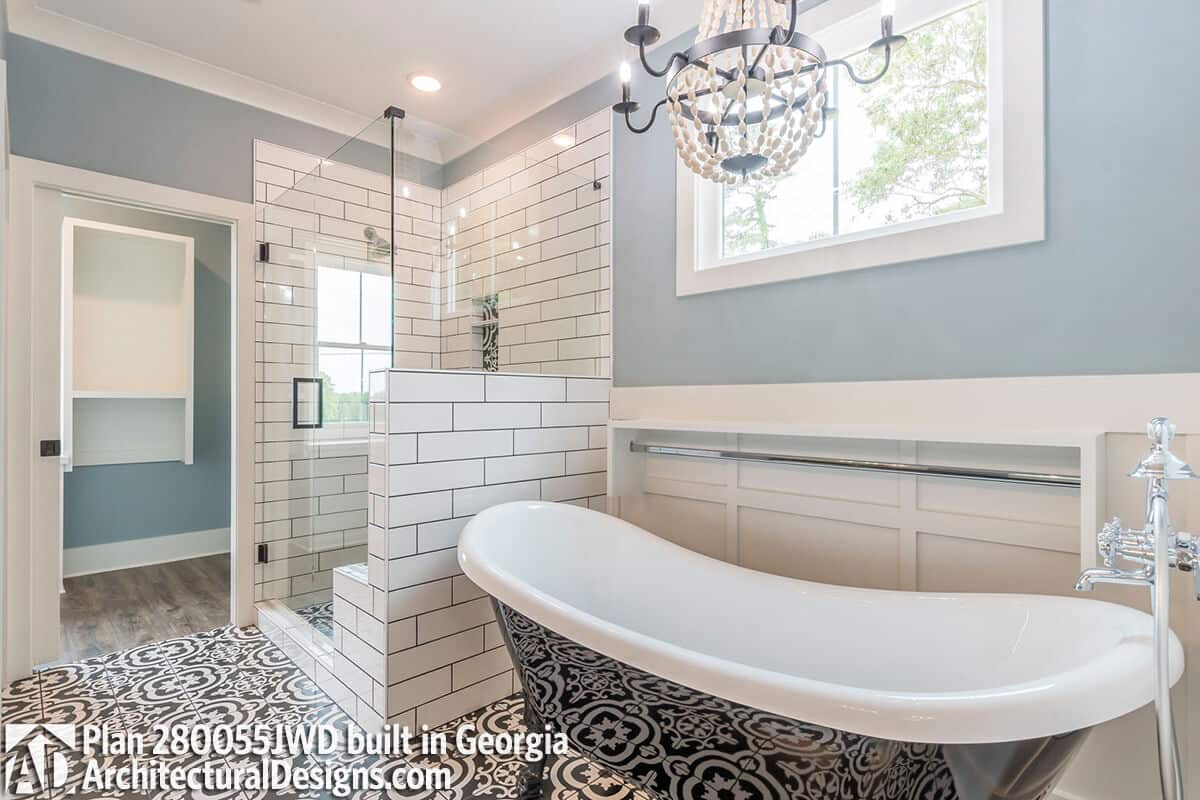 Primary bathroom with a tiled shower and a freestanding tub illuminated by a wrought iron chandelier and a picture window.