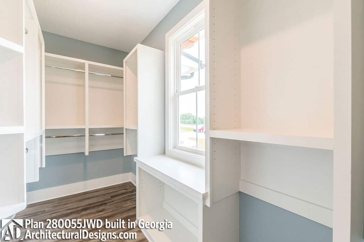 Primary walk-in closet with built-in shelves and table under the framed window.