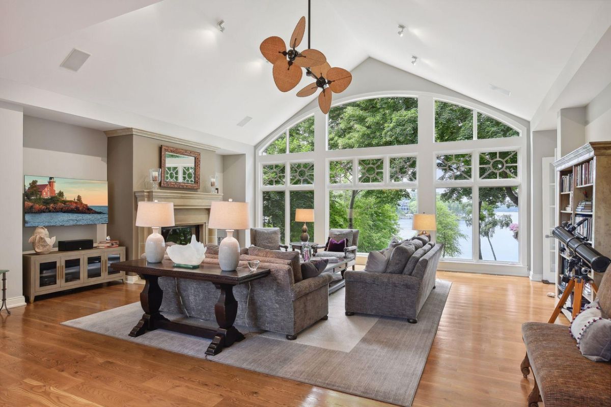 Living room with couches, wood flooring, large glass windows and a fireplace.