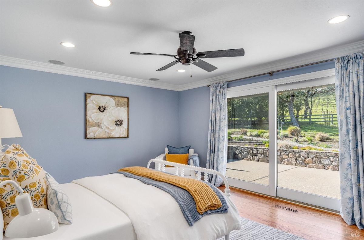 Bedroom with a ceiling fan, wooden floors, a large bed, and sliding glass doors.