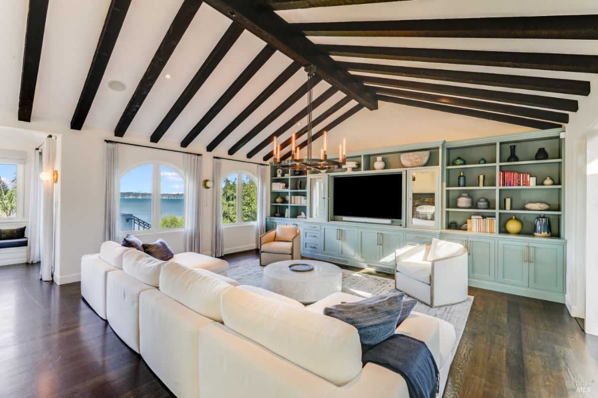 Living room with a chandelier, couches, wooden floors, open beam ceiling and a TV.