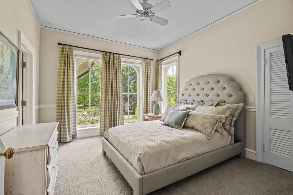 Bedroom with carpet flooring, a ceiling fan, and glass windows.