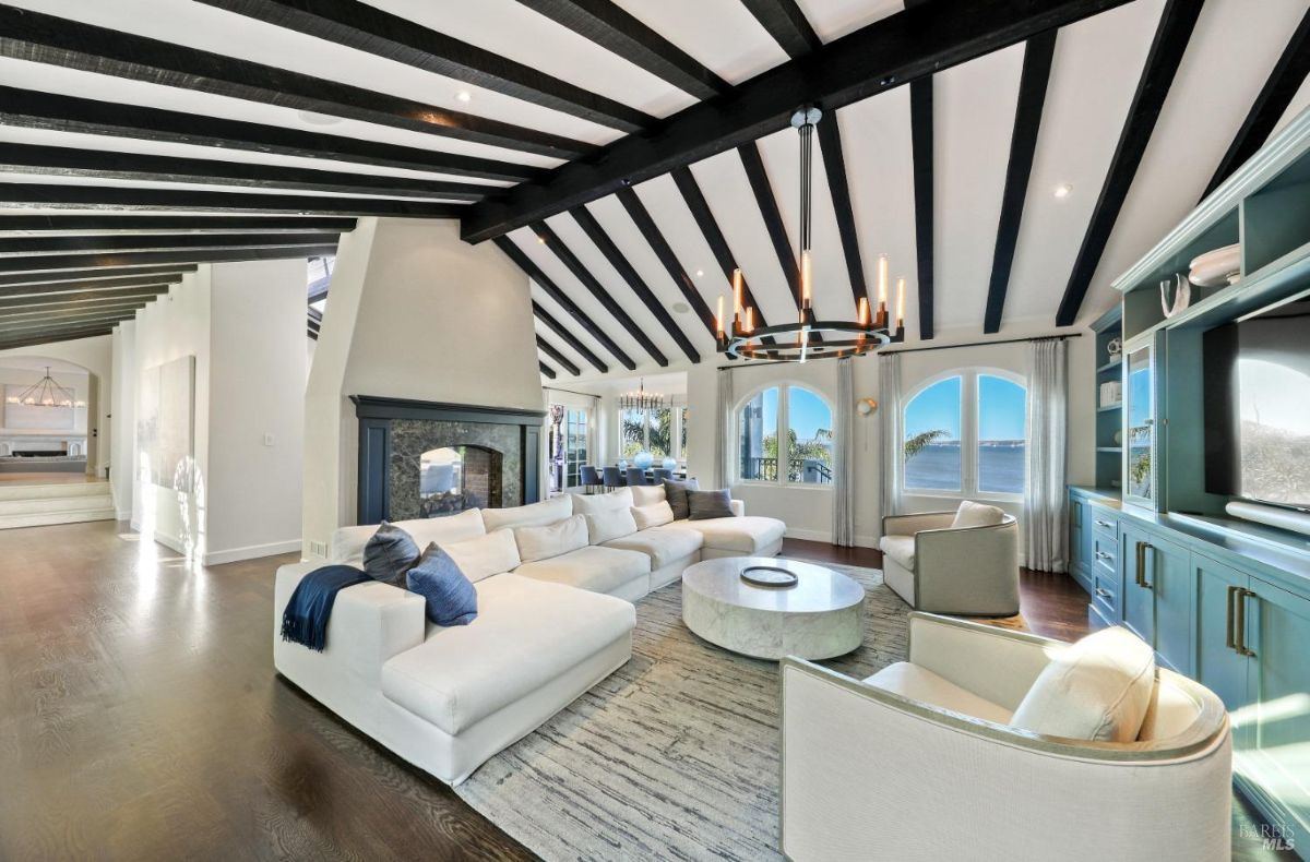 Living room with a chandelier, couches, wooden floors, open beam ceiling and a fireplace.