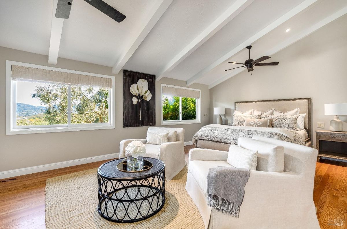 Bedroom with ceiling fans, wooden floors, a large bed, couches and glass windows.