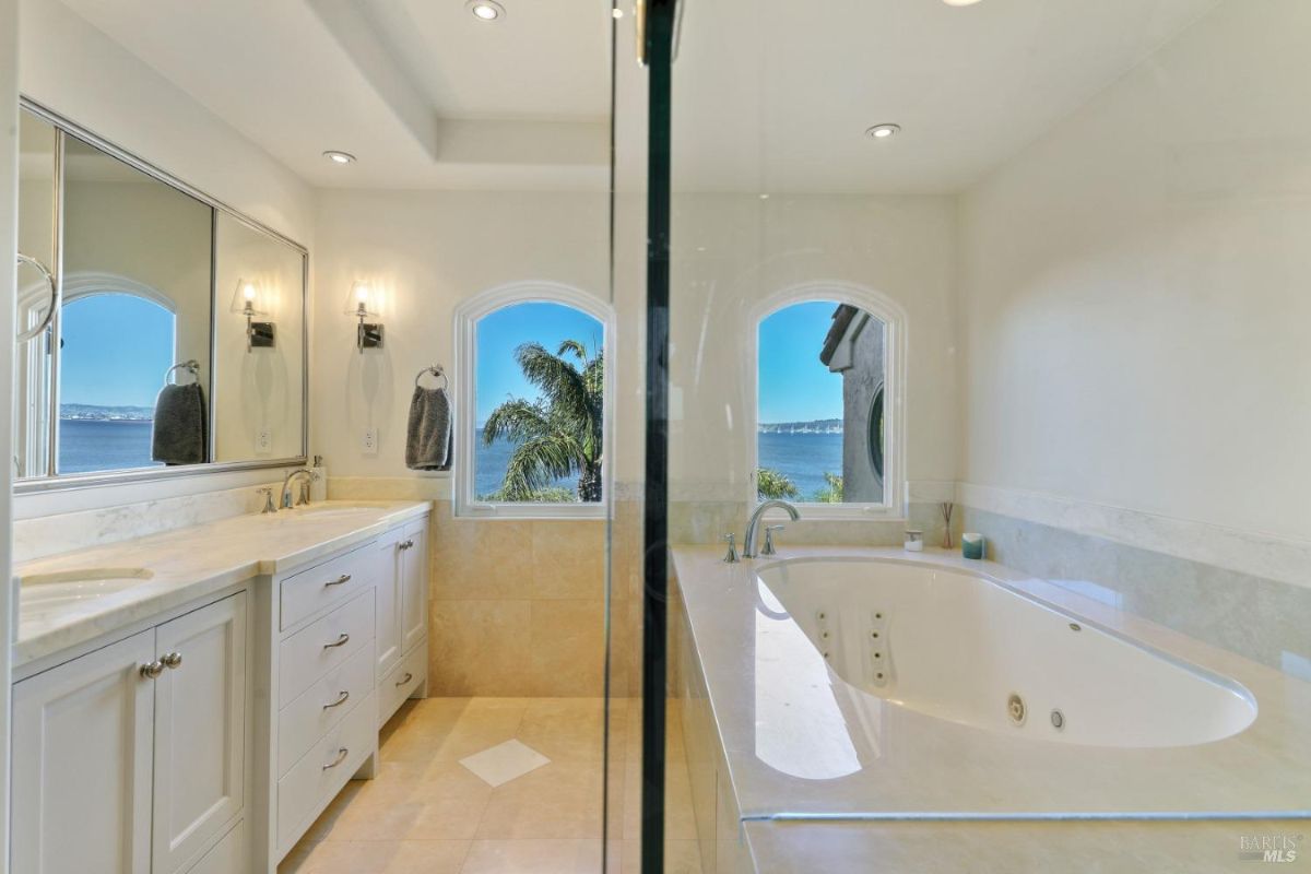 Bathroom with a sink, white cabinets, a large mirror and soaking tub.