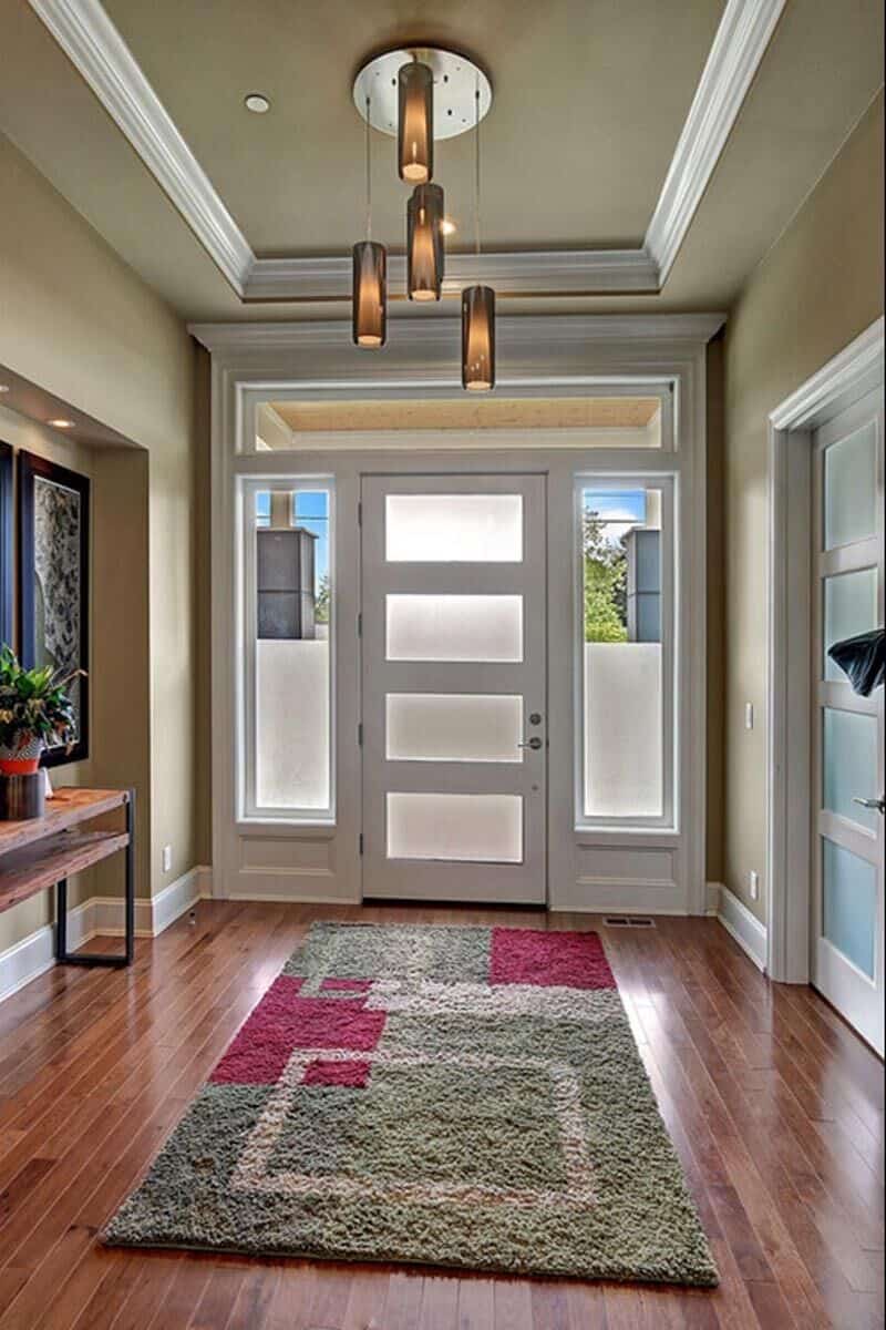 Foyer with a glazed front door, a tray ceiling, and a large rug that lays on the hardwood flooring.