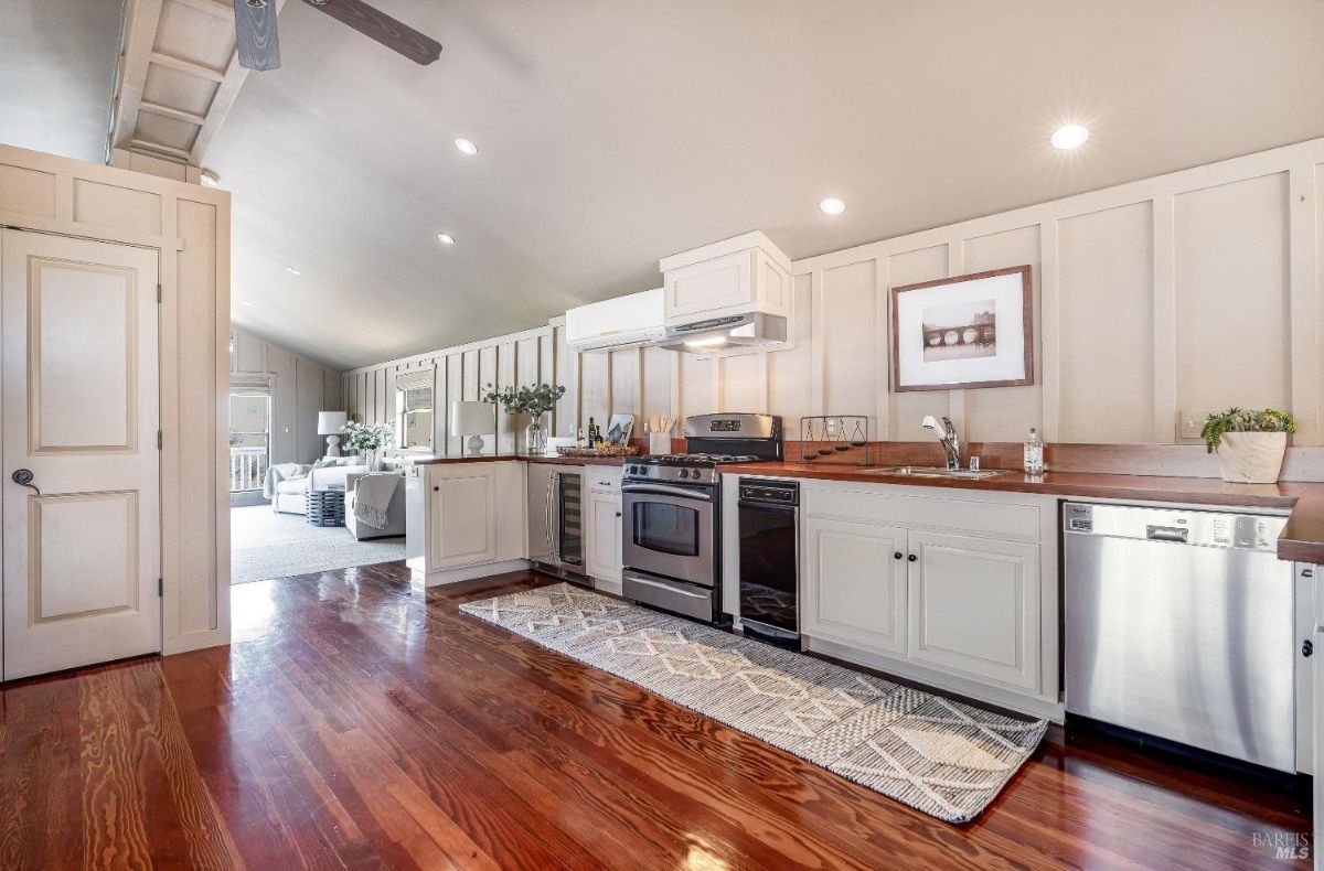 Kitchen with wooden floors, custom lights, custom cabinets and stainless steel appliances.