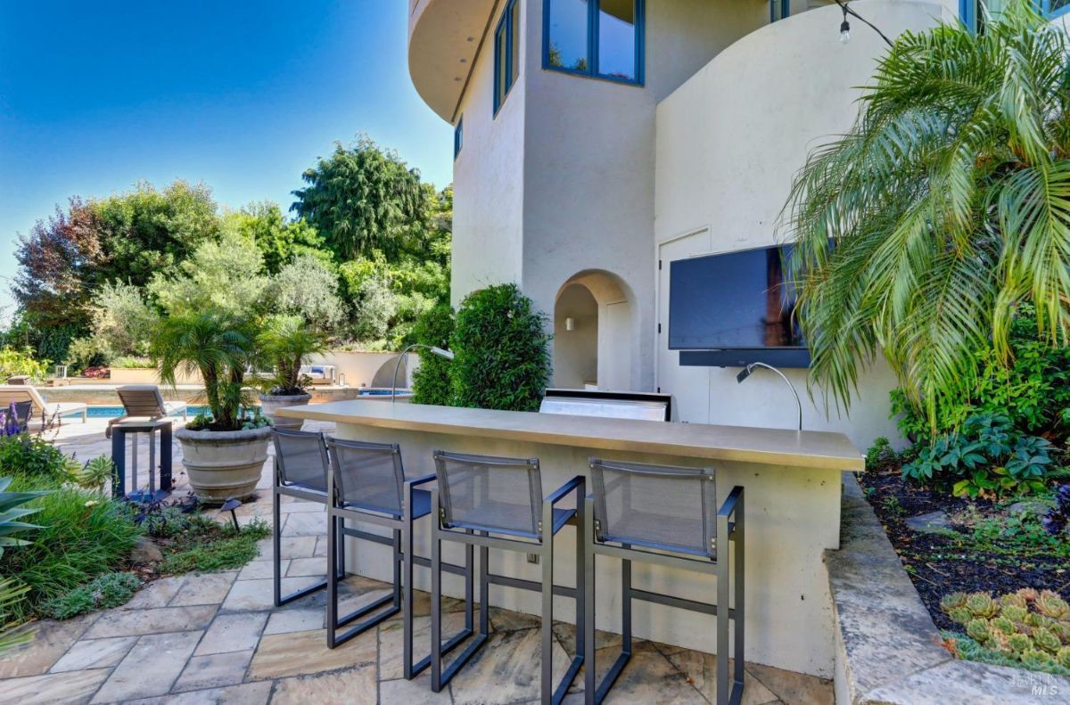 Outdoor kitchen with a bar, high chairs and a TV.