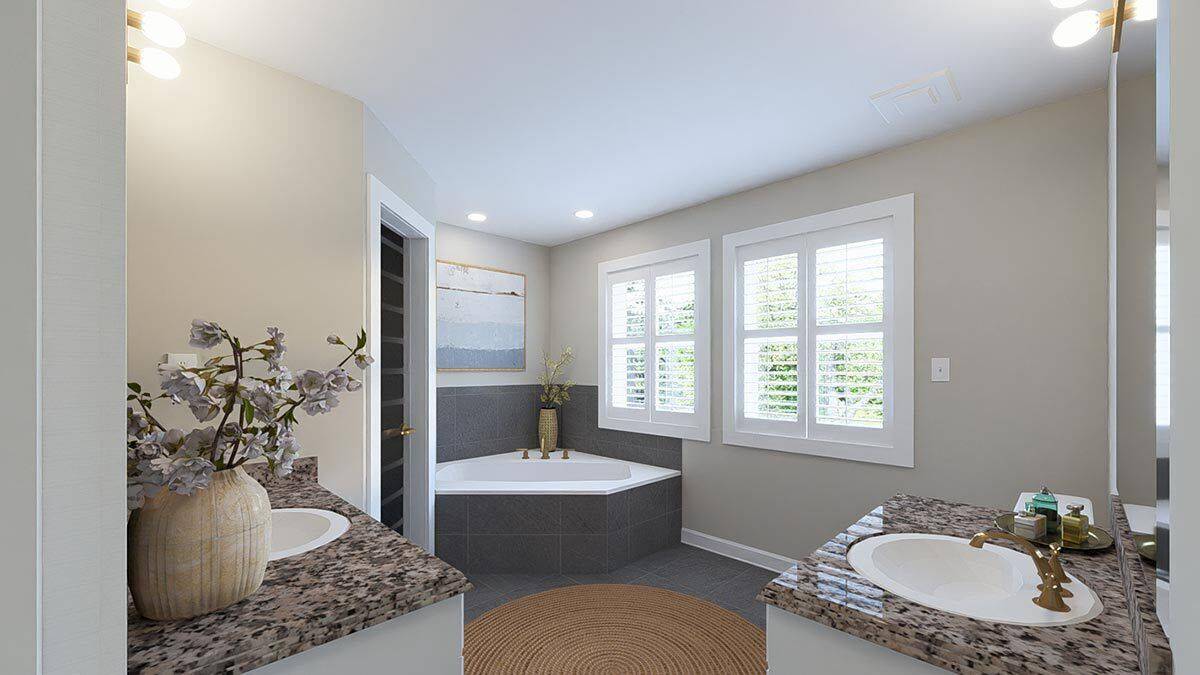 Primary bathroom with his and her vanities and a corner tub illuminated by louvered windows.