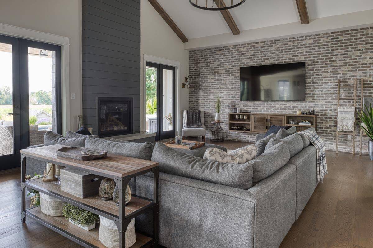 Great room with an electric fireplace, an L-shaped sectional, and a TV mounted against the brick accent wall.