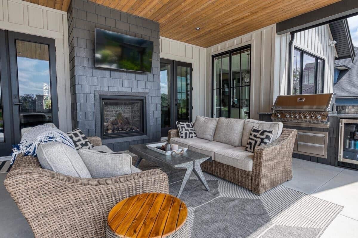 Covered patio with a built-in grill, wicker sofas, and a brick fireplace with a TV on top.