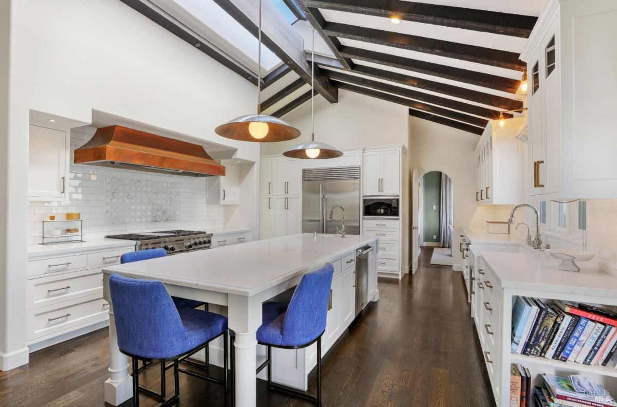 Kitchen with a large island w/sink, marble countertops, skylight and custom cabinets.