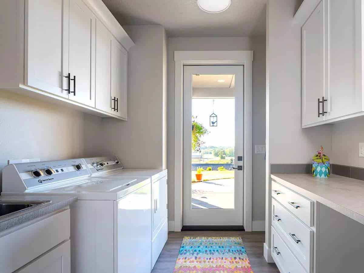 Laundry room with white cabinets, top-load appliances, and outdoor access via a glazed door.