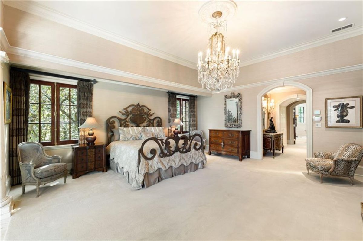 Master bedroom with carpeted flooring, chandelier and a large bed.