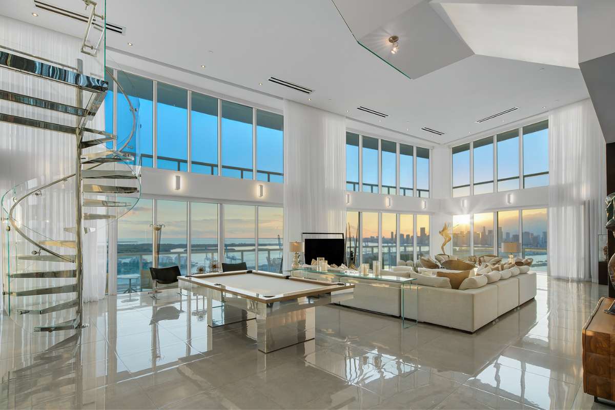 A living room featuring a billiard table and a spiral staircase, surrounded by expansive glass windows