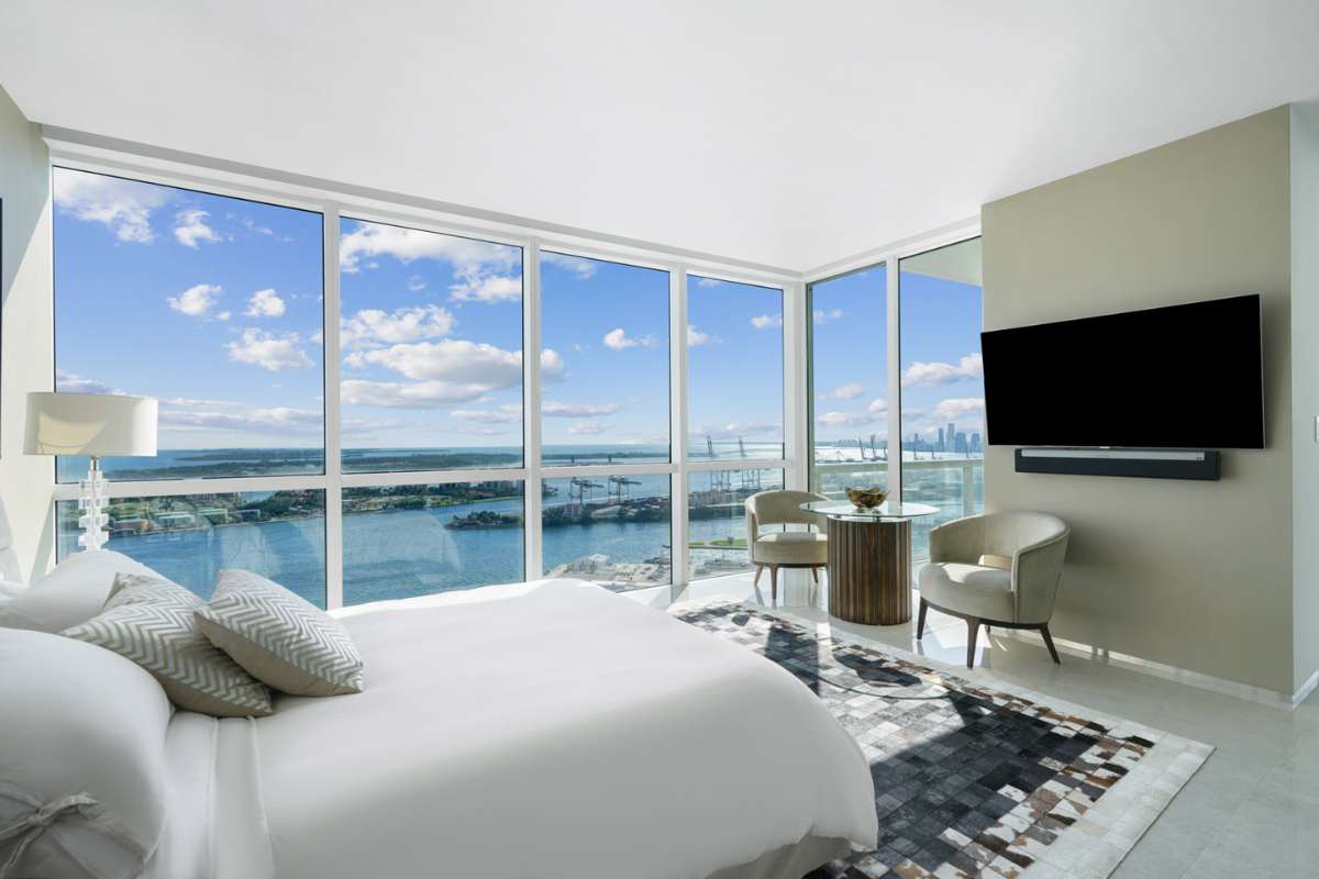 A bedroom with chair, TV and full height glass window