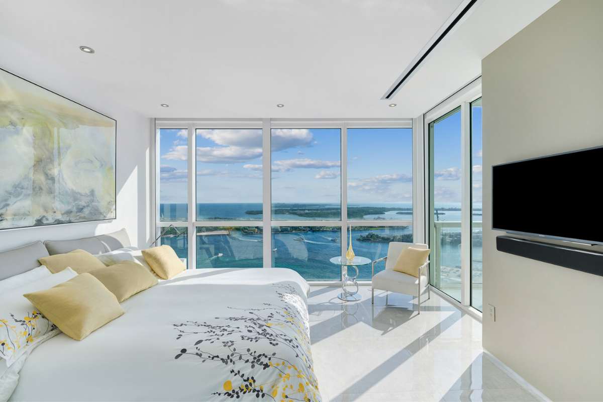 A bedroom with TV surrounded by large window overlooking the ocean