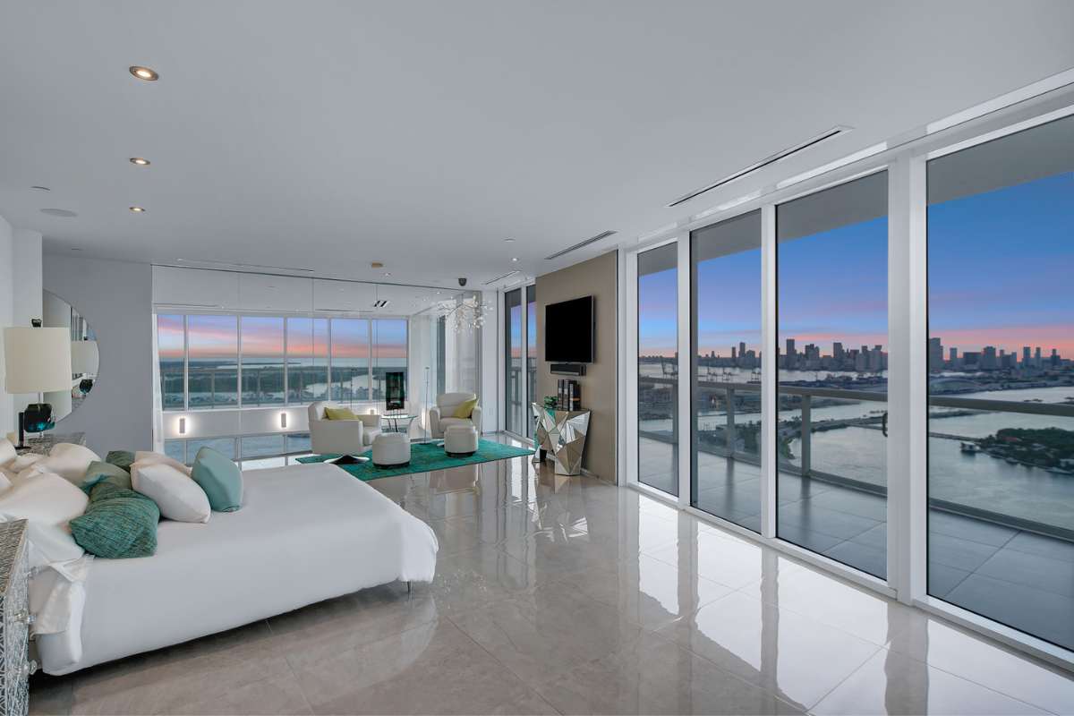 A marble-floored bedroom with a comfortable sitting area, a TV, and surrounded by floor-to-ceiling glass windows