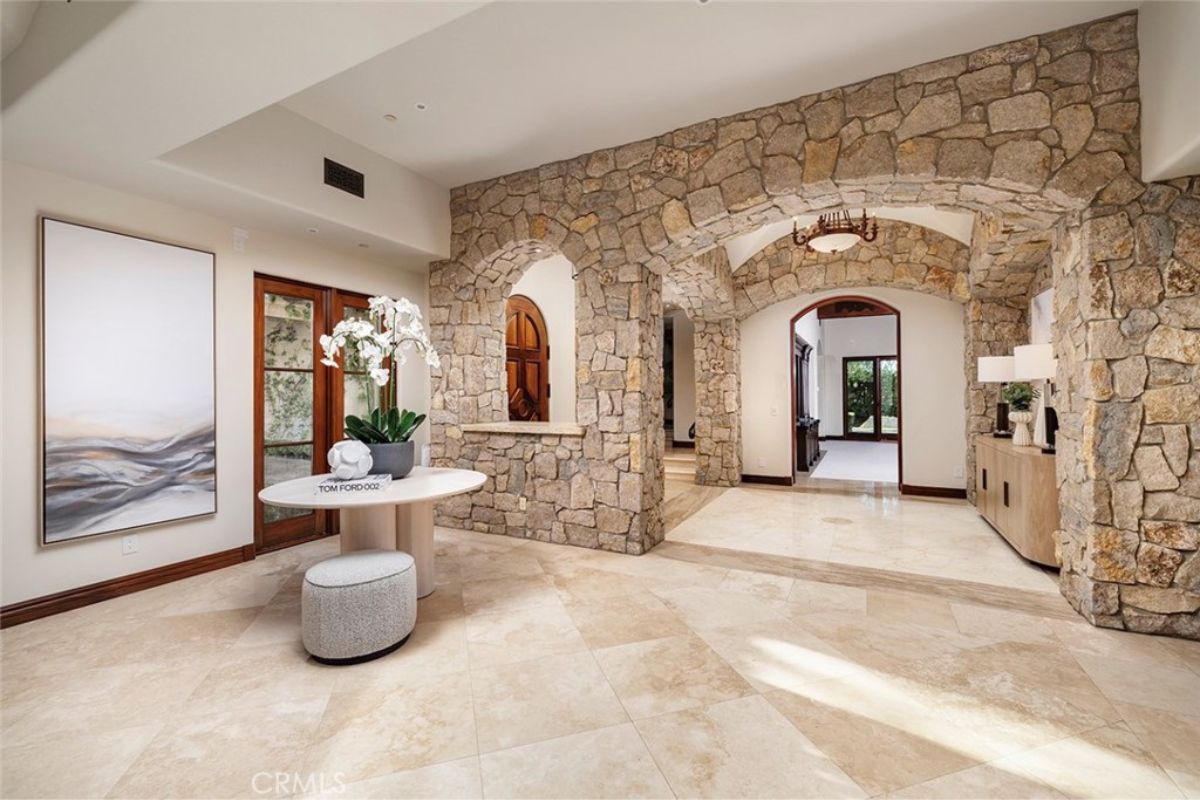 A foyer with tile flooring and a round table with a vase on top.