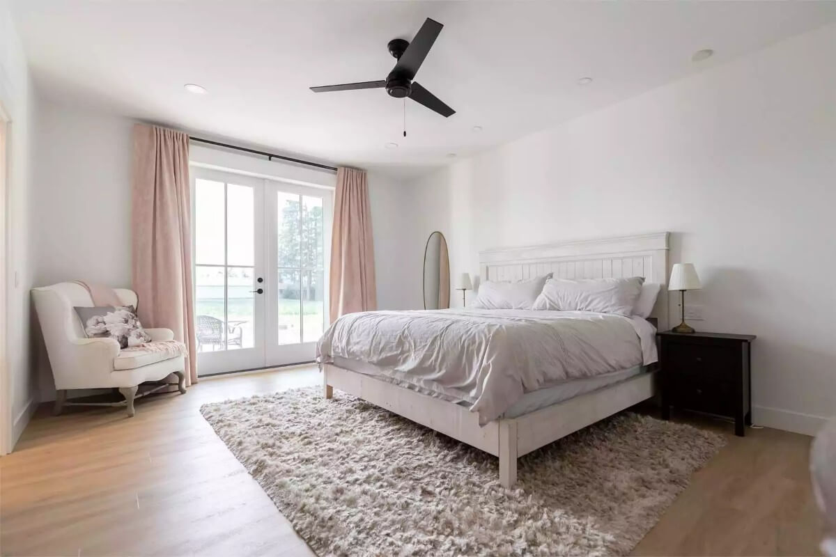 Primary bedroom with a distressed white bed, a wingback chair, and outdoor access via a French door.