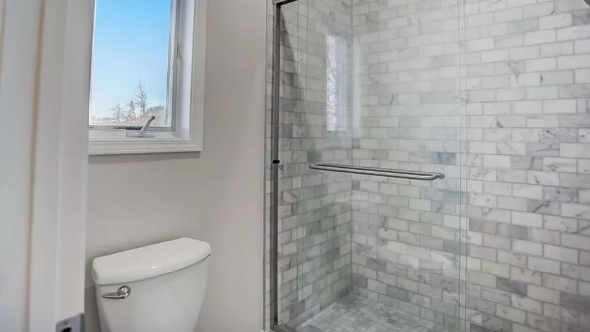 A bathroom with a window, toilet, and shower room.