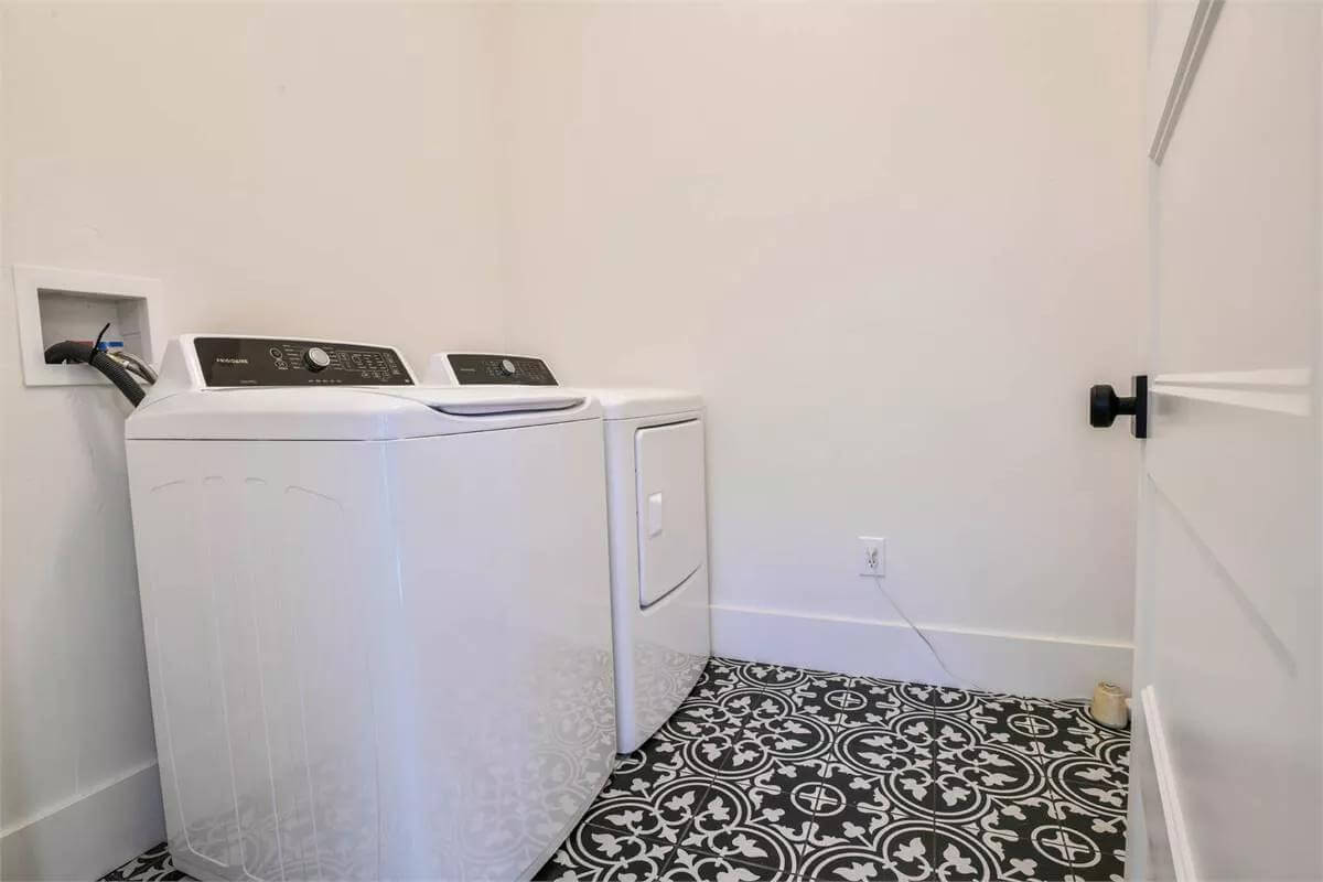 Laundry room with top-load appliances over the decorative tiled floor.