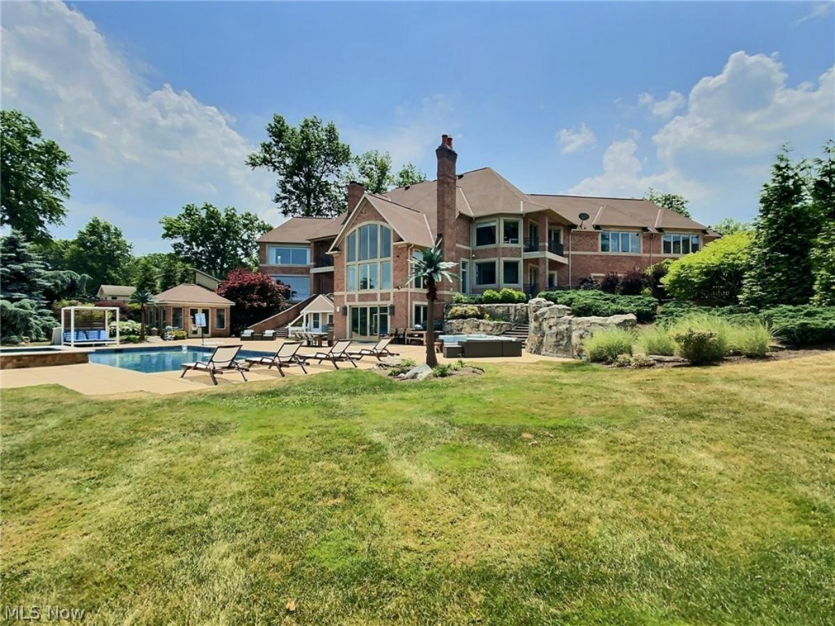 Rear view of the mansion with a pool and a large green lawn.