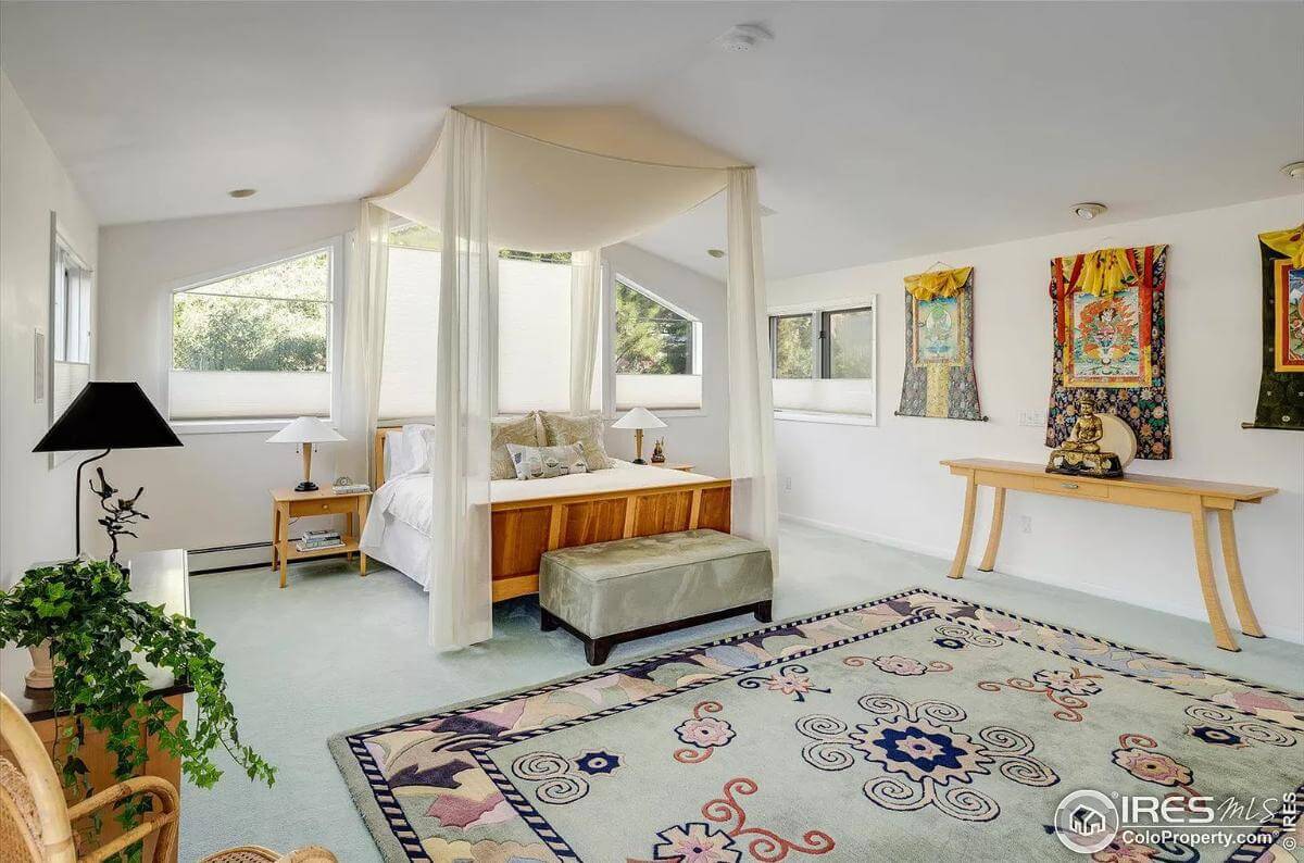 Primary bedroom with a vaulted ceiling, a canopy bed, and colorful artworks adorning the white walls.