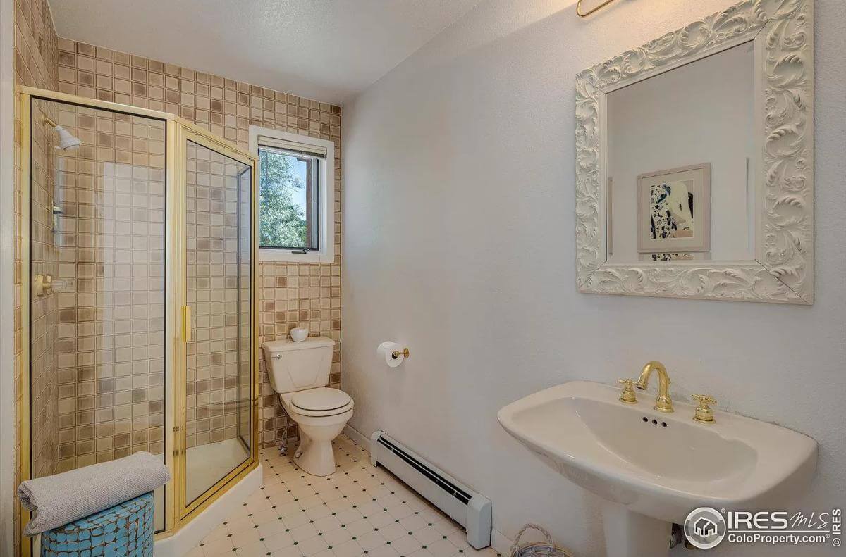 Bathroom with a brass-framed shower and a pedestal sink topped by a white intricate mirror.