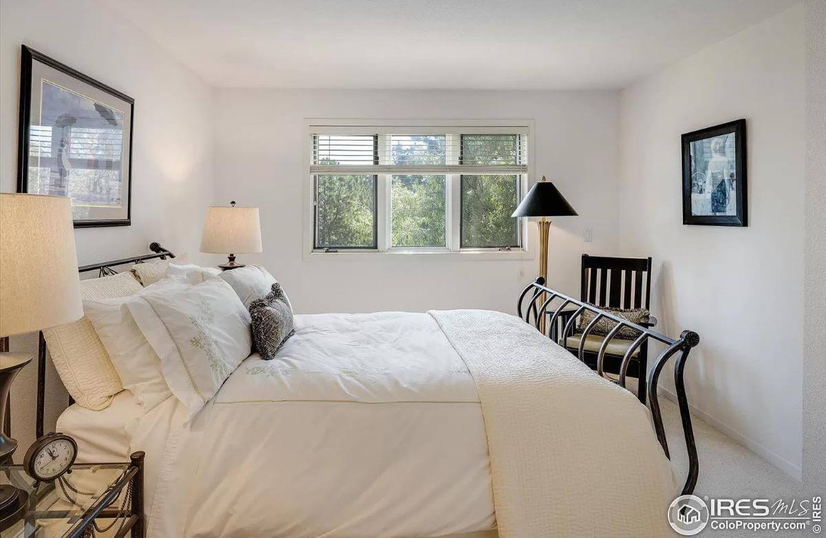 Bedroom with a wrought iron bed and a cushioned chair by the triple windows.