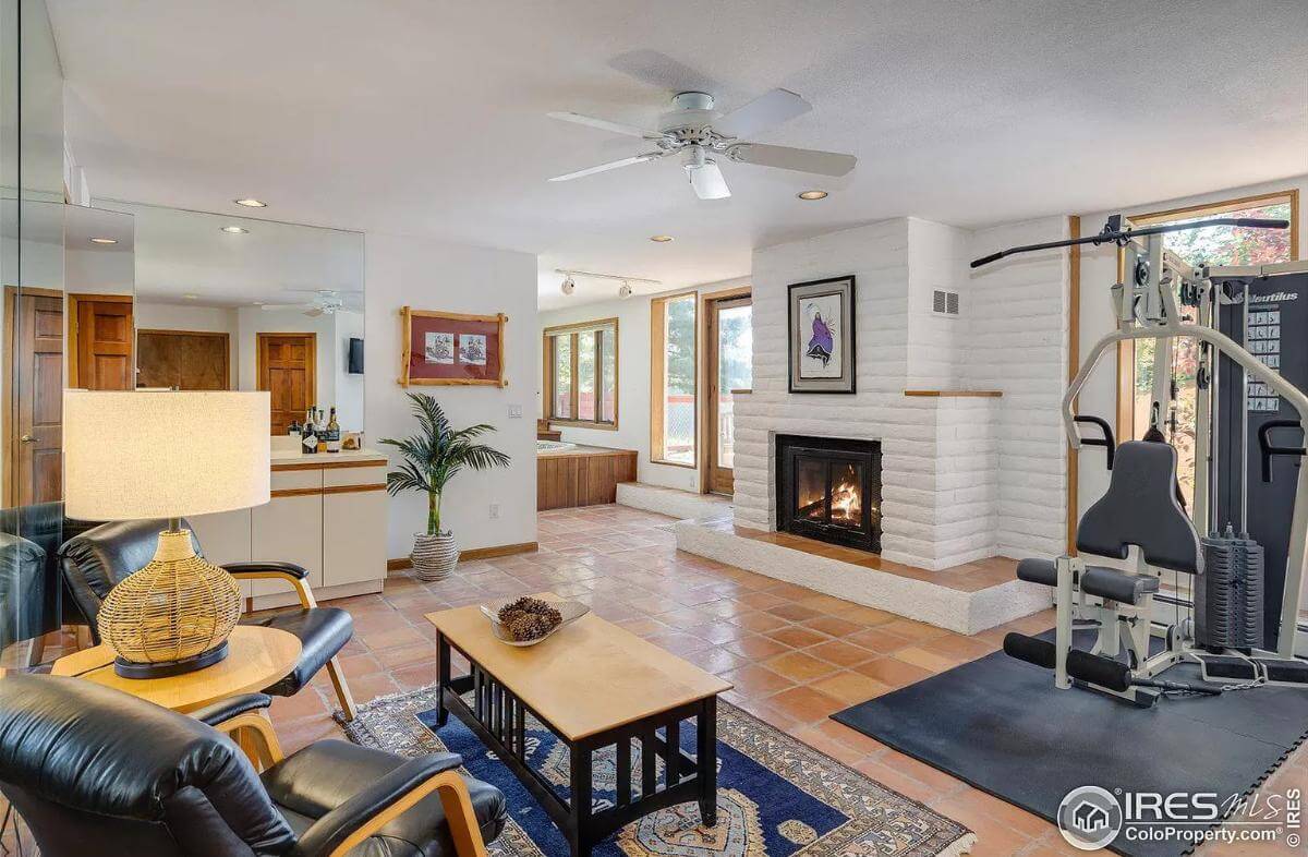 Recreation room with a fireplace, leather chairs, gym equipment, and a bar.