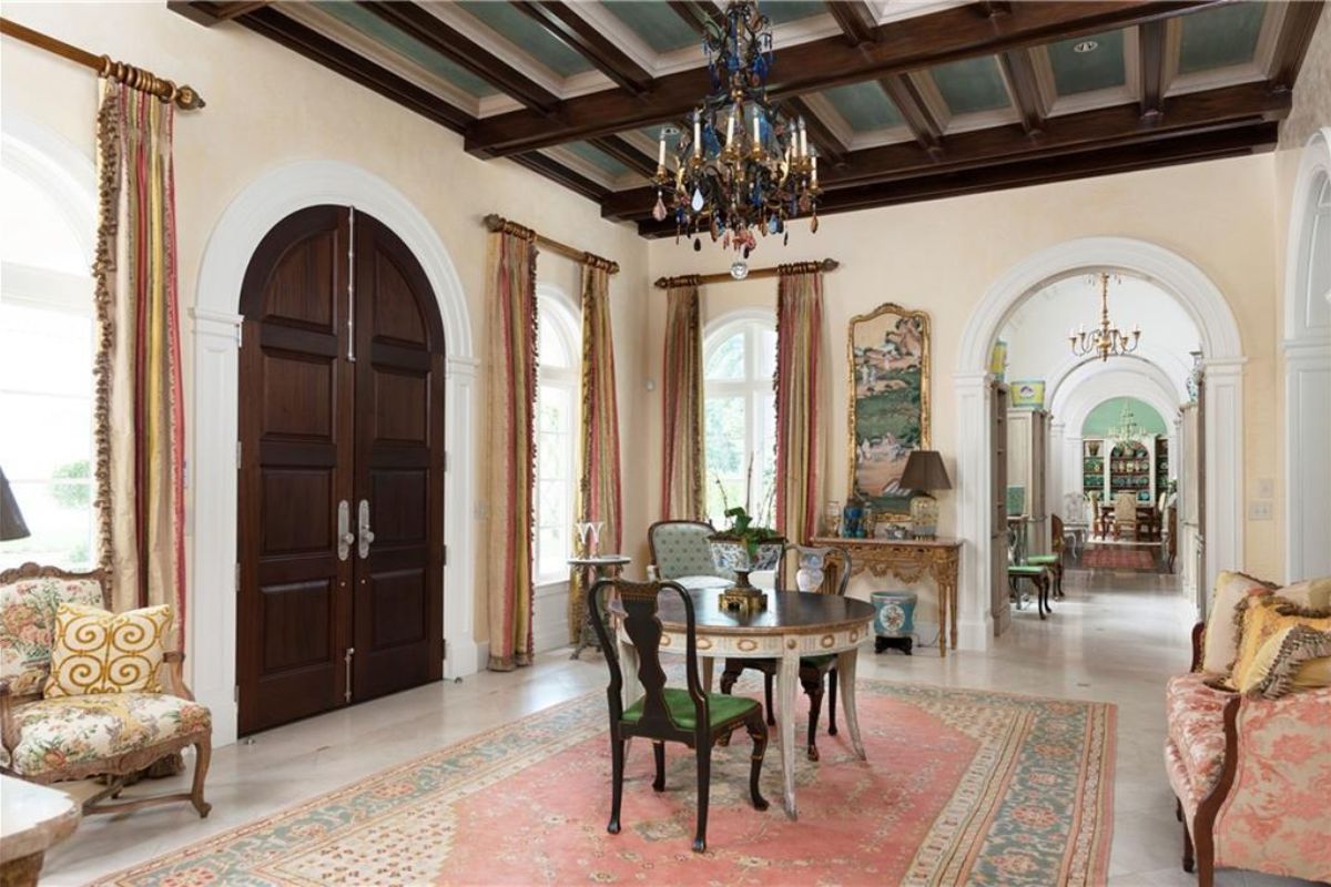 A living room with an exposed beam ceiling, chandelier, rug, chairs, couch, and center table.